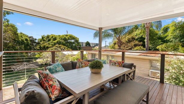An outdoor patio with a wooden table and seating, surrounded by greenery and a clear view of the sky. - Moorooba Pet Friendly Holiday Home Nelson Bay (Nelson Bay)