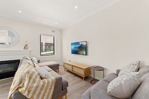 A modern living room with a fireplace, a sofa set, a wooden console table, and a framed landscape painting.