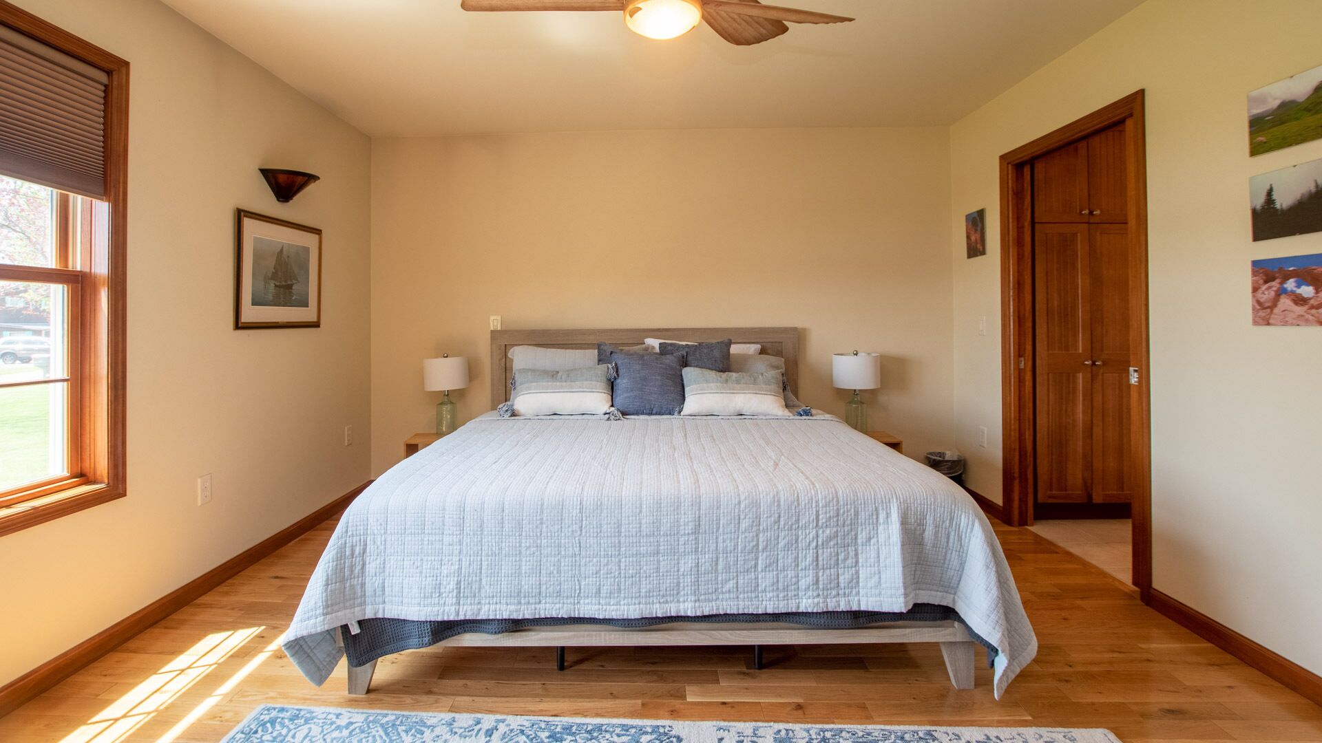 Un dormitorio con cama, dos lámparas de noche, ventilador de techo, ventana con persianas y una puerta.