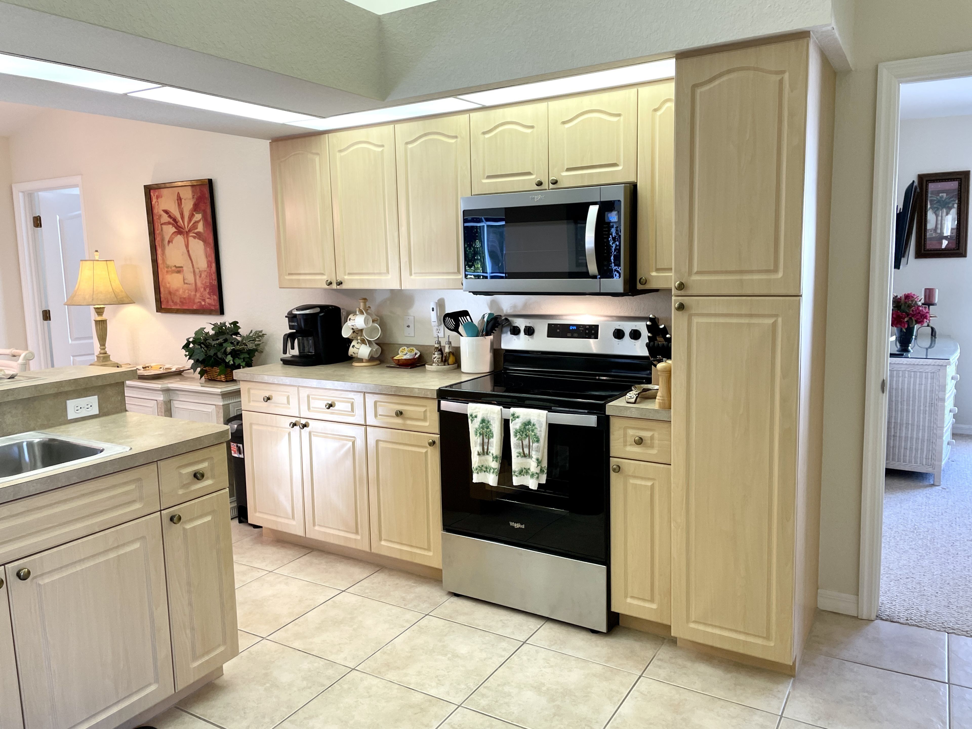 A modern kitchen with light wood cabinets, stainless steel appliances, and a tiled floor.