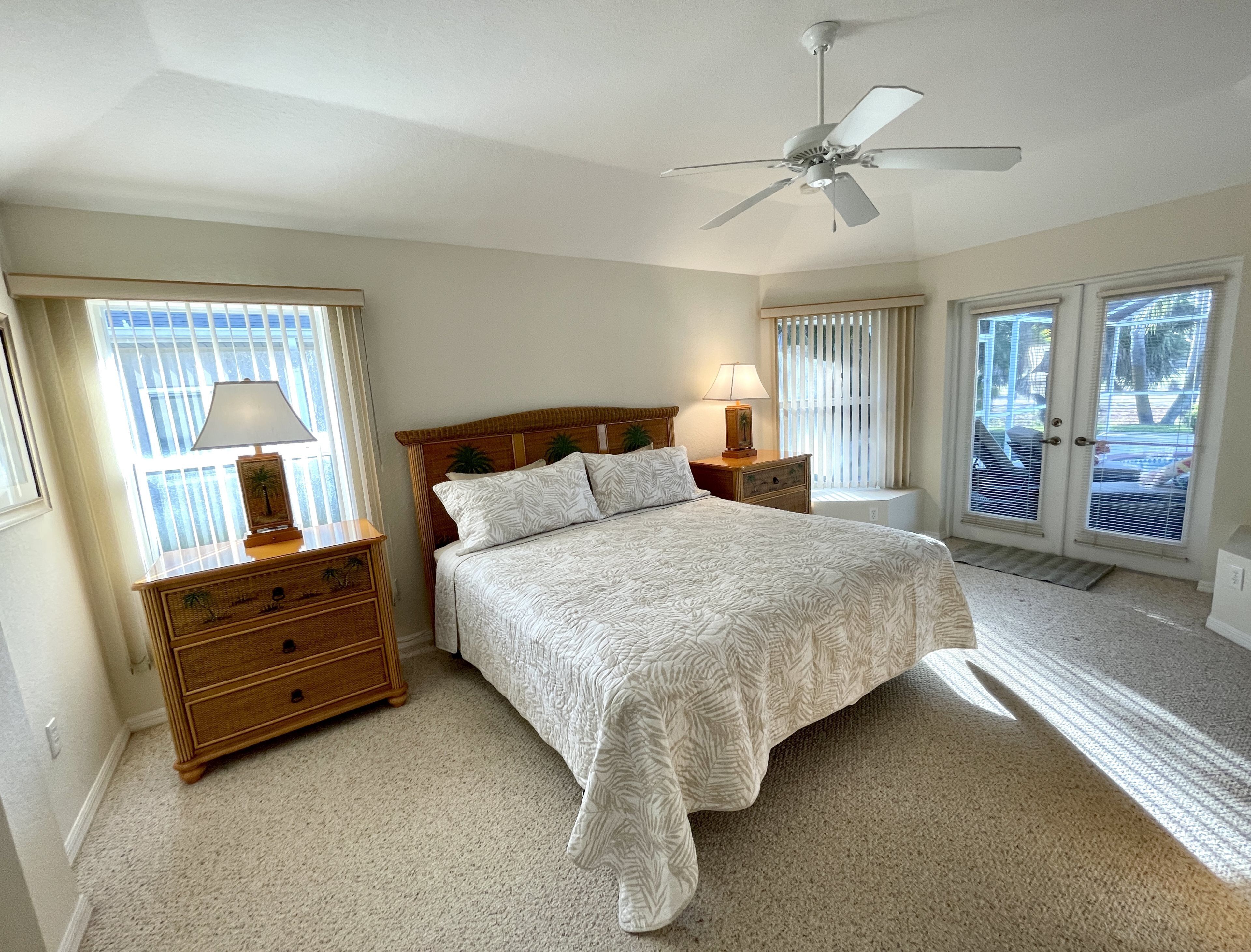 A bedroom with a bed, nightstands, a ceiling fan, and a view through the glass doors.