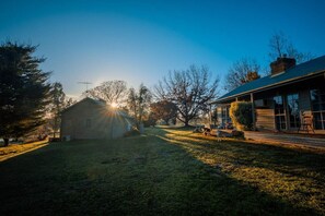 Een rustieke chalet met een houten gevel, een veranda met buitenmeubilair en een grote boom op de achtergrond.