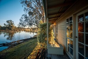 Une propriété située au bord d’un lac, dotée d’une terrasse en bois, d’un porche couvert et offrant une vue sur l’eau.