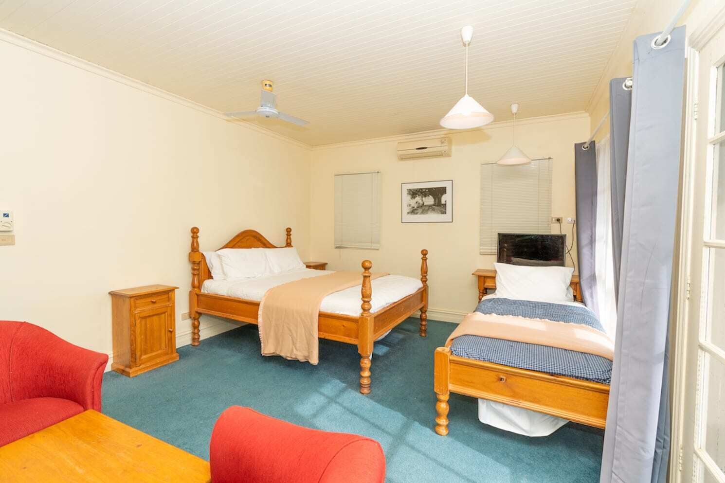 A bedroom with two wooden beds, a small wooden cabinet, a red chair, a yellow table, and a television.