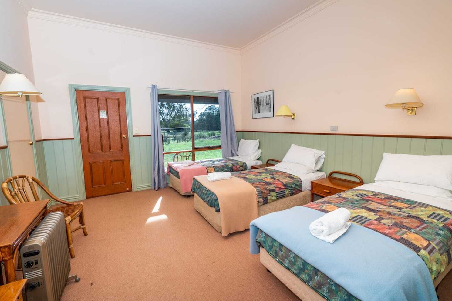 Een hotelkamer met twee bedden, een houten stoel, een tafel, een radiator en een raam met uitzicht op de omgeving.