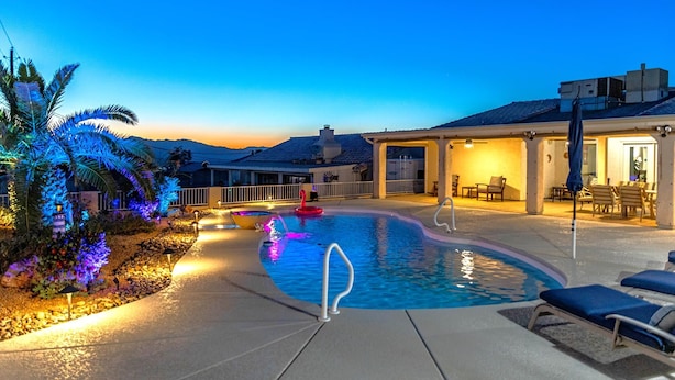A swimming pool with a curved edge, a lounge area with chairs, and a covered patio area. - Tropical Heated Pool & Sunset Views Oasis (Lake Havasu City)