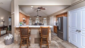 A kitchen with a central island, two bar stools, a refrigerator, and wooden cabinets. - Tropical Heated Pool & Sunset Views Oasis (Lake Havasu City)
