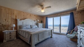 Une chambre avec un lit, une commode, une table de chevet, un ventilateur de plafond et une vue sur la plage.