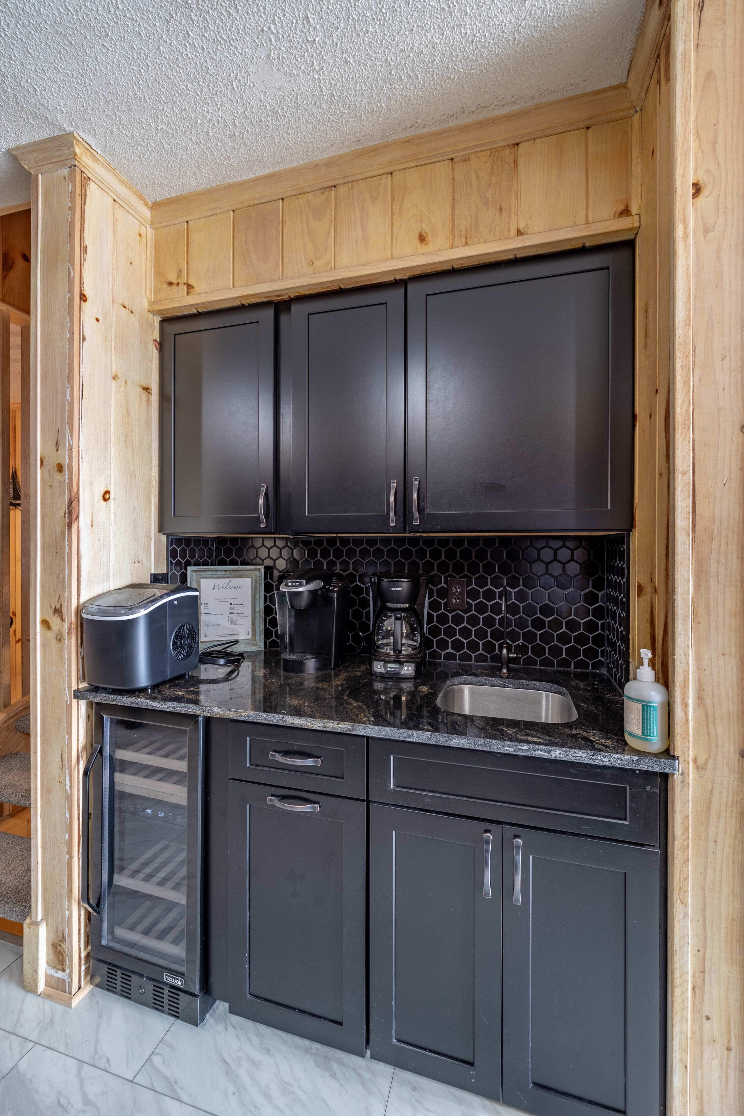 A kitchen with dark cabinets, a toaster, a coffee maker, a sink, and a refrigerator.