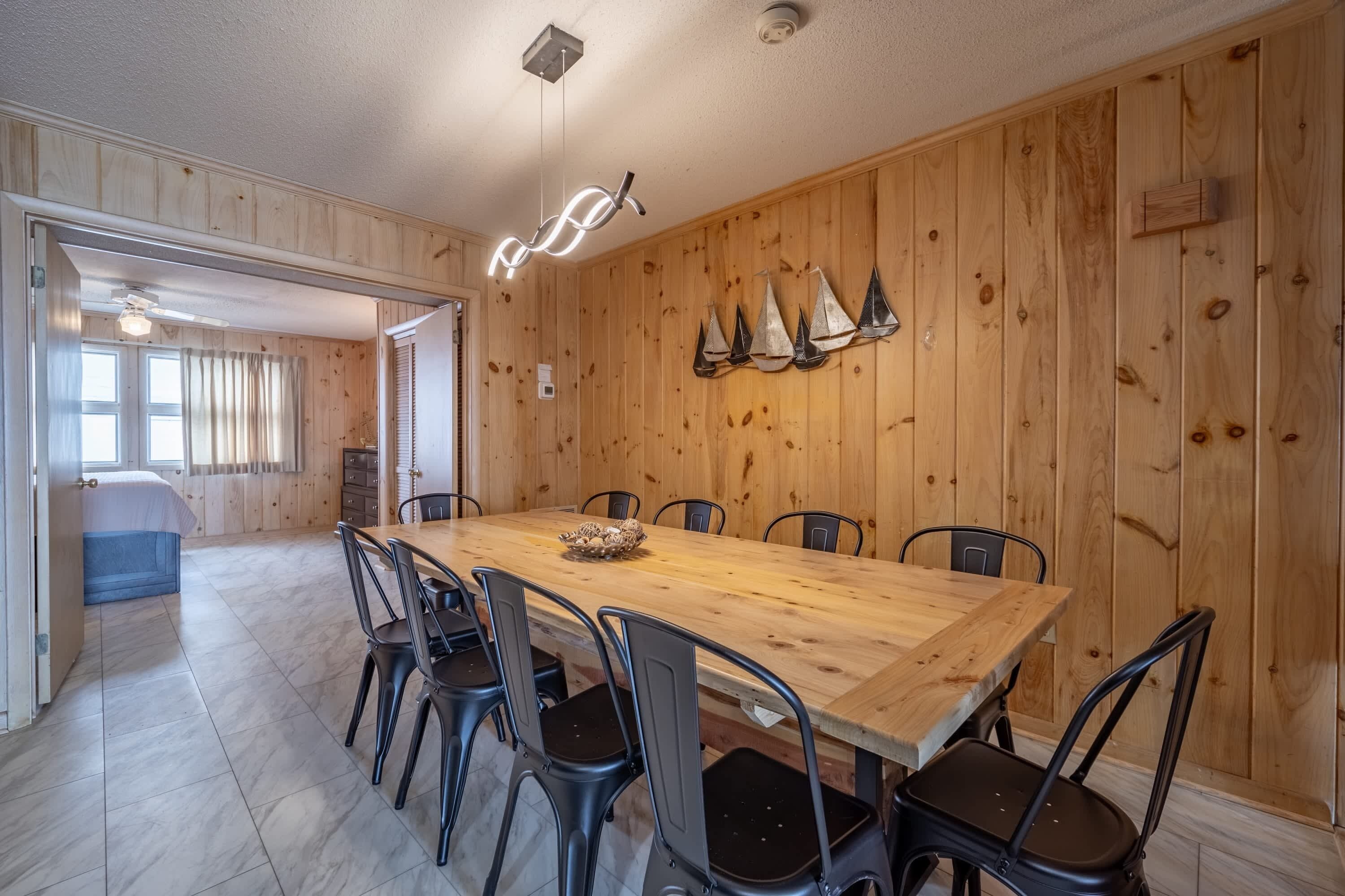 Zona pranzo con tavolo e sedie in legno, un lampadario a sospensione e un addobbo a parete.