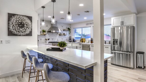 Una cocina moderna con una isla grande, electrodomésticos de acero inoxidable, iluminación colgante y un salpicadero geométrico.