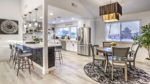 Una cocina moderna con una isla central, taburetes de bar y un comedor con candelabro.