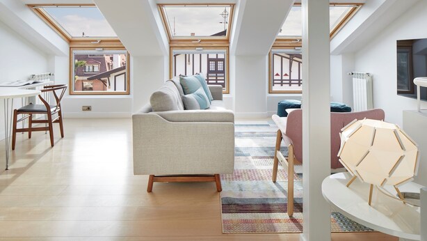 A spacious loft apartment with high ceilings, skylights, a modern sofa, a dining area, and a view of the neighborhood. - Villa Loretopea by FeelFree Rentals (San Sebastián)