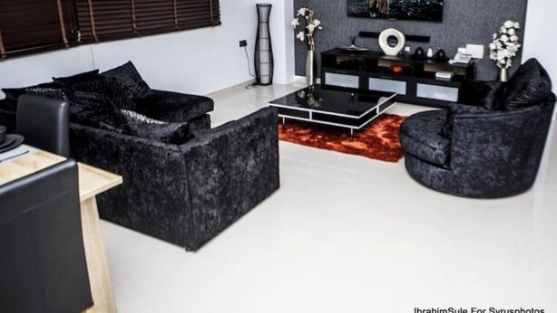 A modern living room with black sofas, a flat-screen TV, and a minimalist decor. - High End Newly Refurbished 6th Floor Apartment (Lekki)