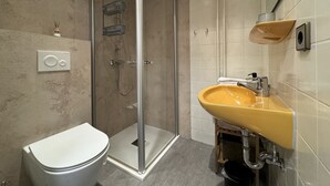 A bathroom with a glass-enclosed shower, a white toilet, and a yellow sink with a mirror above it. - Ferienhaus Möhrle 1 (Ueberlingen)