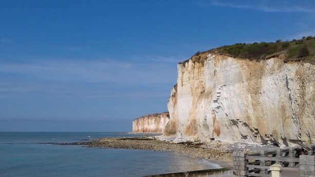 A coastal cliff with a rocky shoreline and a clear sky.
