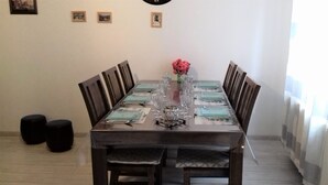 A dining table set for six with chairs, a vase with flowers, and a clock on the wall.