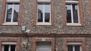 A two-story building with a stone facade, multiple windows, and a central door with a number plaque.