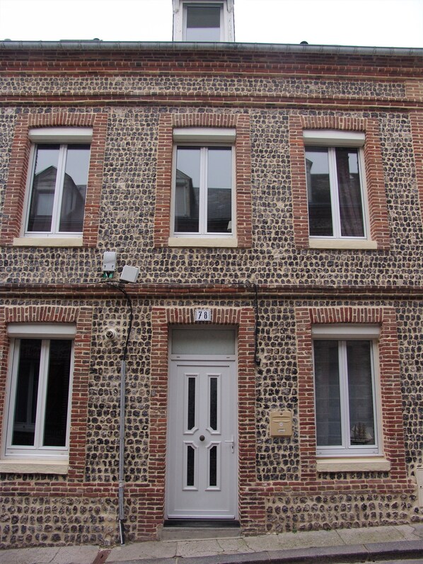 A two-story building with a stone facade, multiple windows, and a central door with a number plaque.
