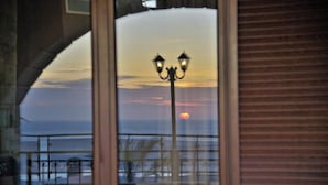 Tramonto visibile attraverso una finestra, con ringhiera del balcone e lampione di strada.