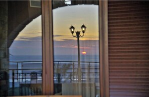 A sunset view through a window with a balcony railing and a street lamp.