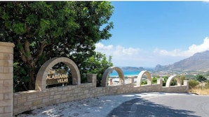 Un ingresso in pietra con il cartello 'NEW ALASSARNA VILLAS' e vista sul paesaggio.