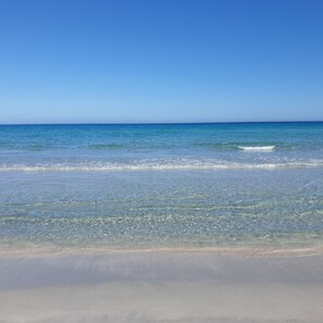 Une plage avec une eau d’un bleu limpide et un rivage sablonneux.