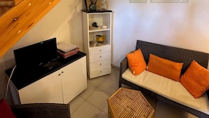 Een gezellige woonkamer met een trap, een bank met oranje kussens, een klein houten tafeltje en een witte kast met decoratieve objecten.