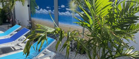 Relax in a serene outdoor space with a beach mural, lounge chairs, and a potted plant.
