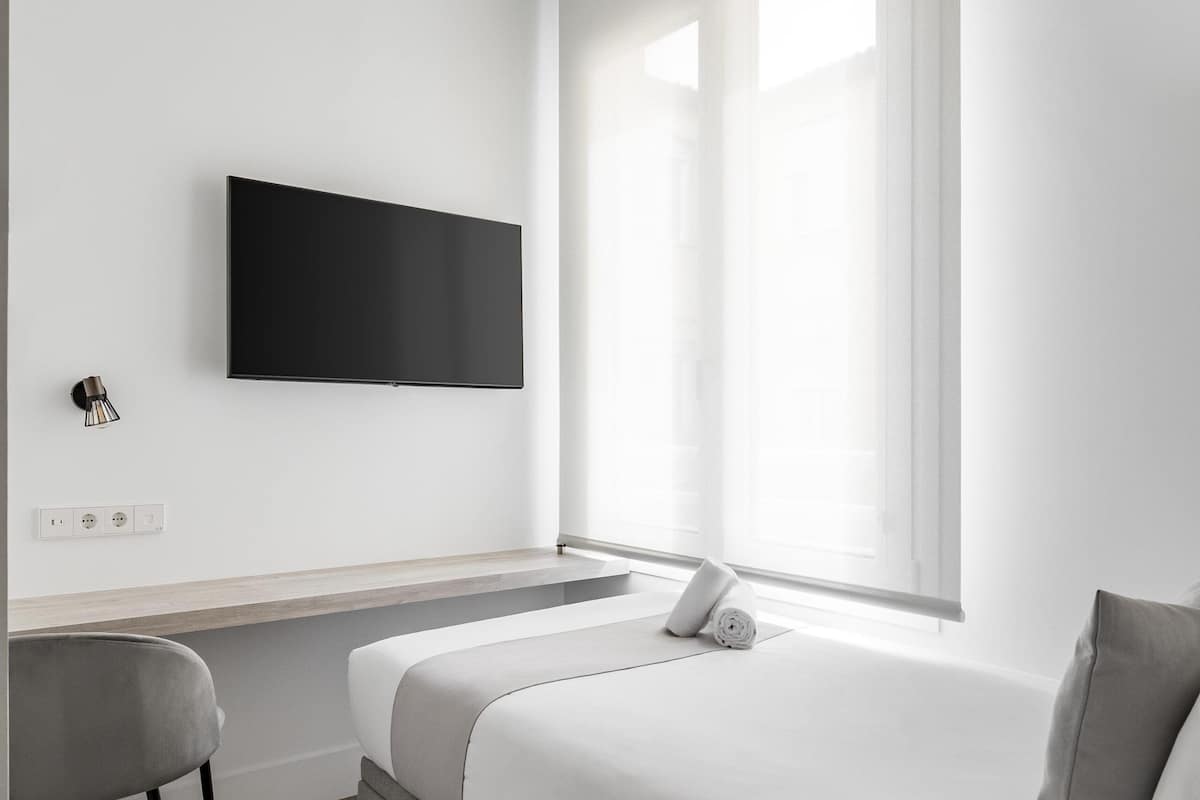 Une chambre d’hôtel minimaliste, comprenant un lit, un bureau et un téléviseur fixé au mur.