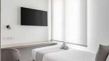 Een minimalistisch hotelkamer met een bed, een bureau en een aan de muur bevestigde televisie.