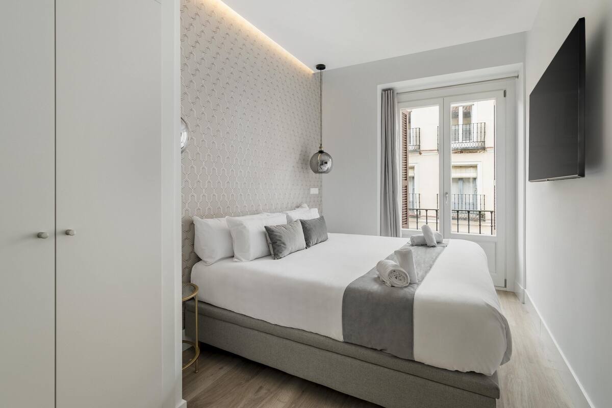 Une chambre moderne avec un grand lit, une table de chevet, un téléviseur fixé au mur et une vue sur le balcon.