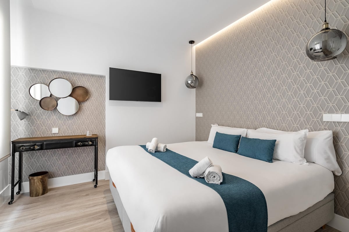 Une chambre d’hôtel moderne avec un grand lit, une table de chevet, une télévision et un miroir fixé au mur.