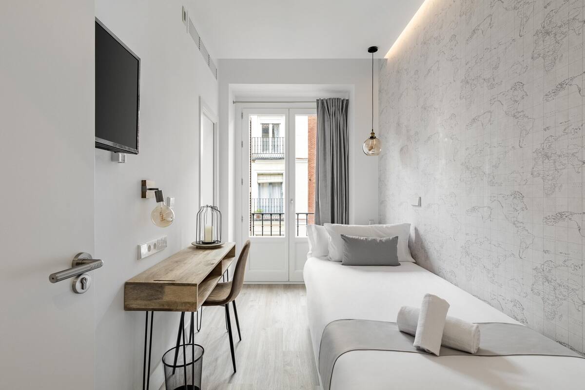 Une chambre d’hôtel moderne, équipée d’un lit, d’un bureau et offrant une vue sur le balcon extérieur.