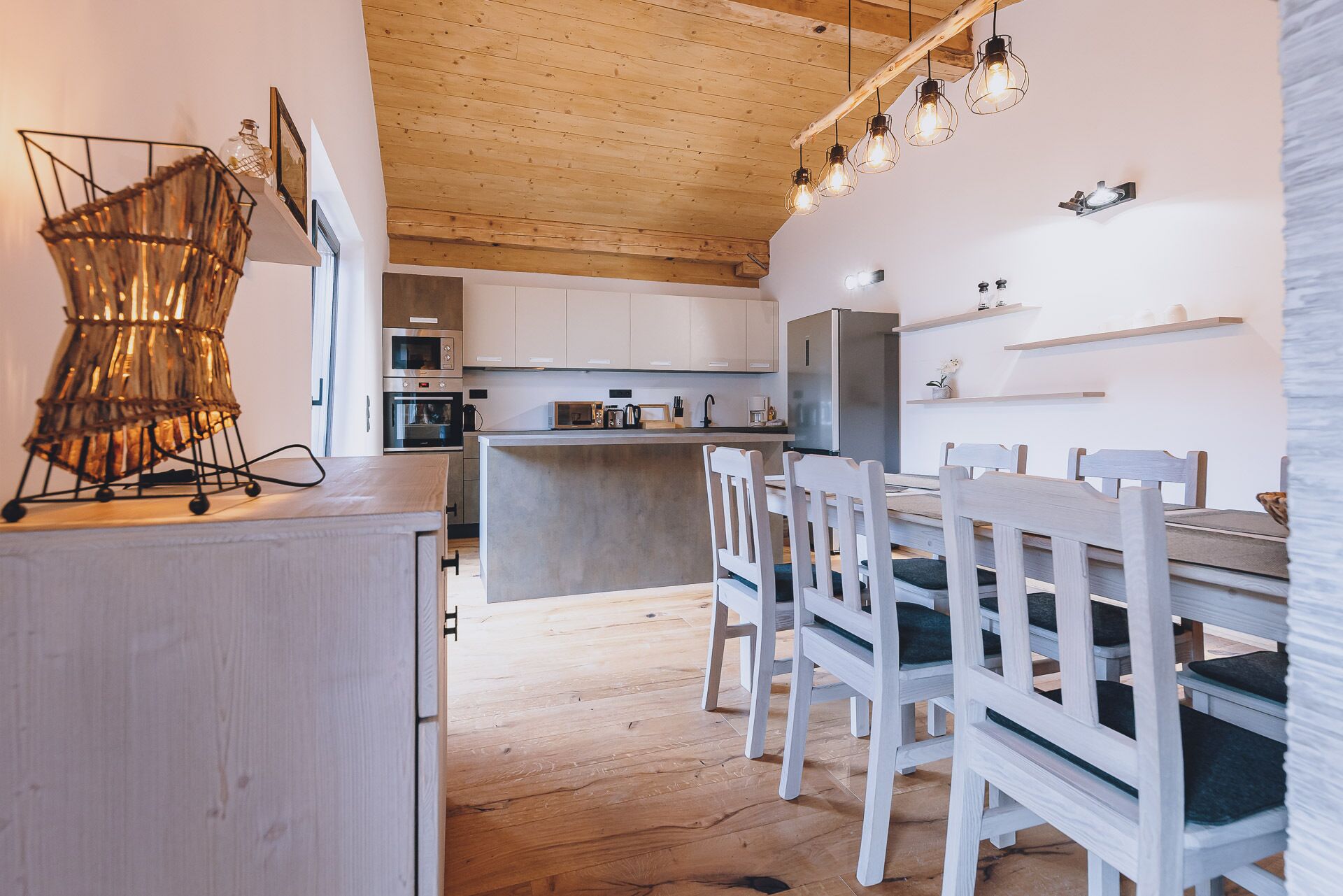 A modern kitchen with wooden cabinets, a central island, and a dining area with white chairs.