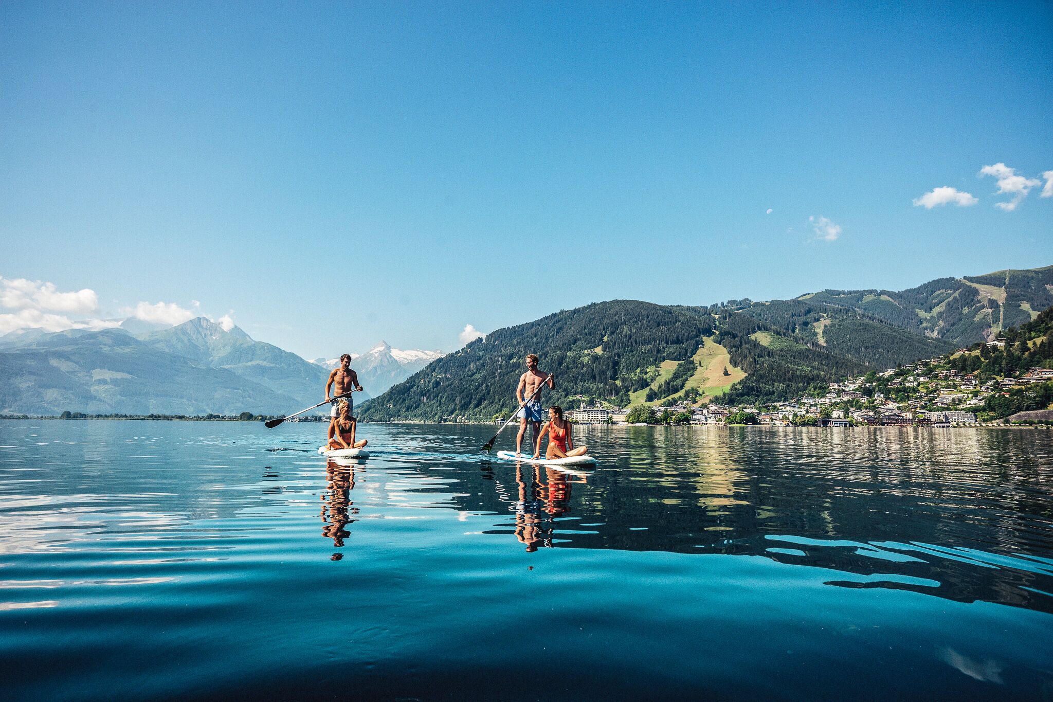 Two people paddleboarding on a calm lake with mountains in the background.