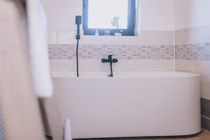 Um banheiro moderno com uma banheira independente, uma janela sobre a pia e um painel de azulejos.