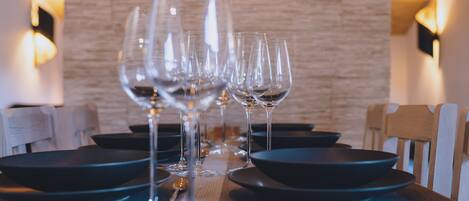 A dining table set with multiple wine glasses and plates, with a wooden wall and wall-mounted lights in the background.