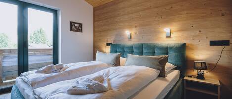 A double bed with two pillows and a blanket, a bedside table with a lamp, and a wooden headboard.