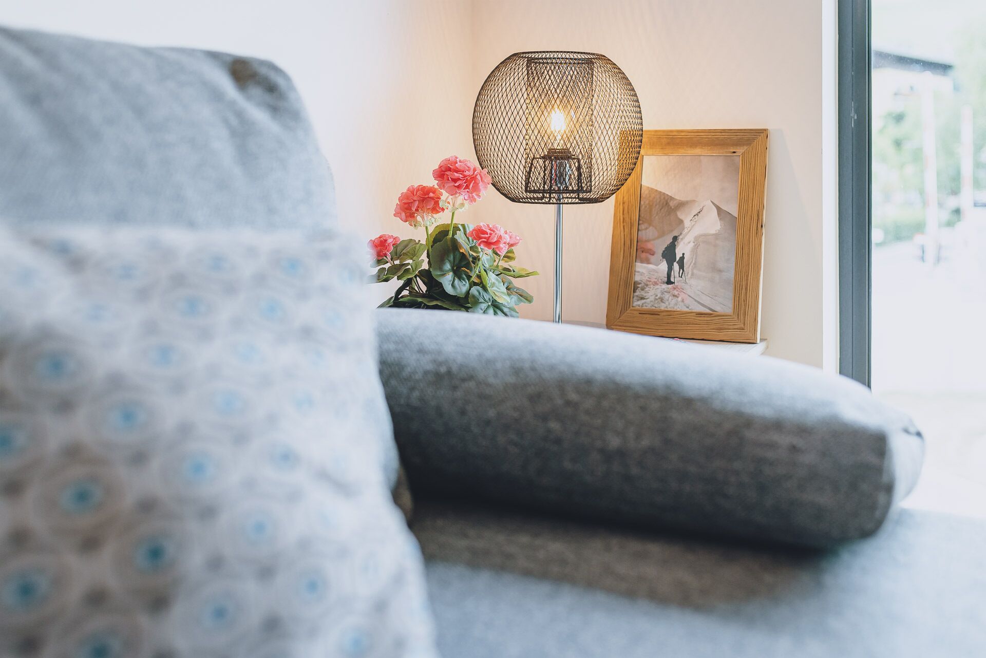 Une pièce chaleureuse avec un canapé gris, une lampe décorative et un tableau encadré posé sur une table d’appoint.