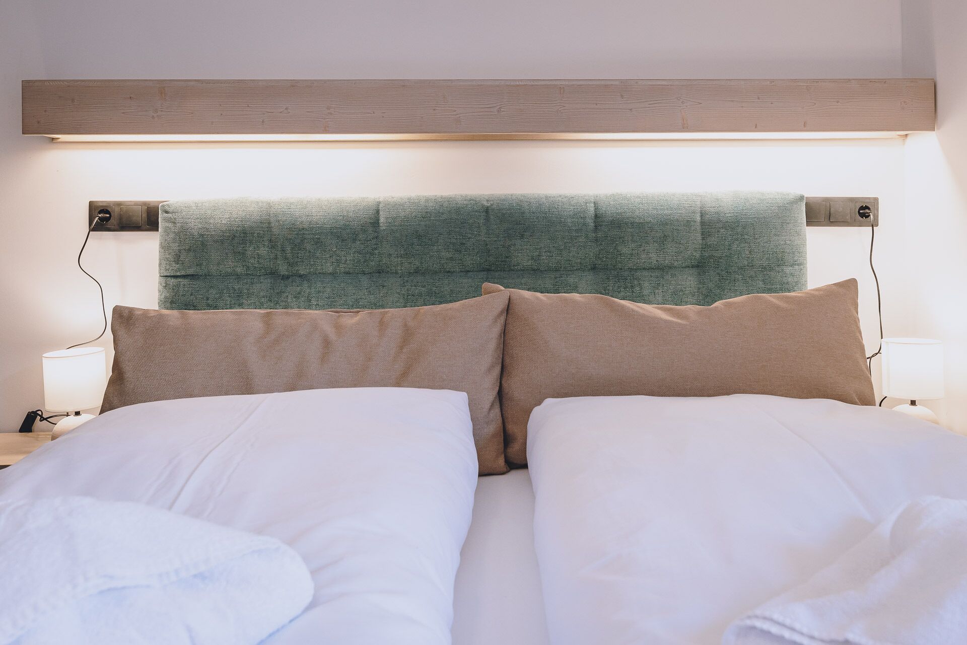 Un lit bien fait, avec du linge de lit blanc et deux oreillers beige, une tête de lit en bois et des lampes de chevet.