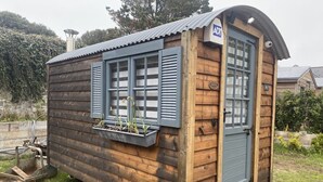 Una cabaña de madera con un pequeño porche, una puerta y una ventana con contraventanas.