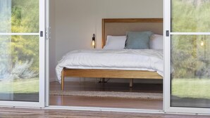 Een slaapkamer met een houten bed, wit beddengoed en uitzicht door glazen deuren.