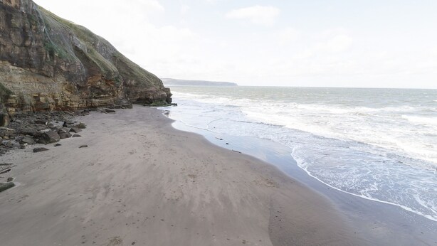 Een strand met een rotsachtige klif en rustige golven.