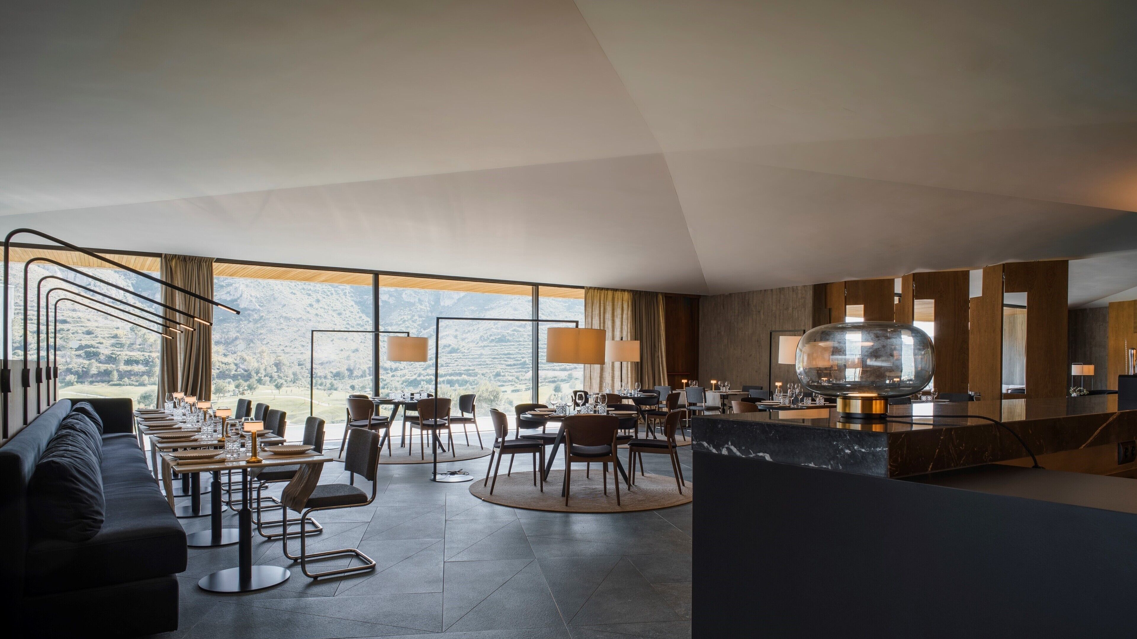 Een modern restaurantgedeelte van een hotel met een groot raam met uitzicht, een bar en een zithoek met tafels en stoelen.