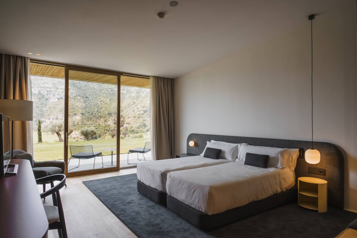 A modern bedroom with two beds, a desk, and a large sliding glass door leading to an outdoor area.