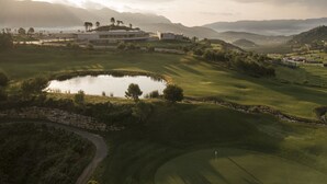 A golf course with a pond, a stone wall, and a building with a flat roof.
