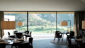 A dining area with tables set for four, large windows offering a view of rolling hills and a mountain.