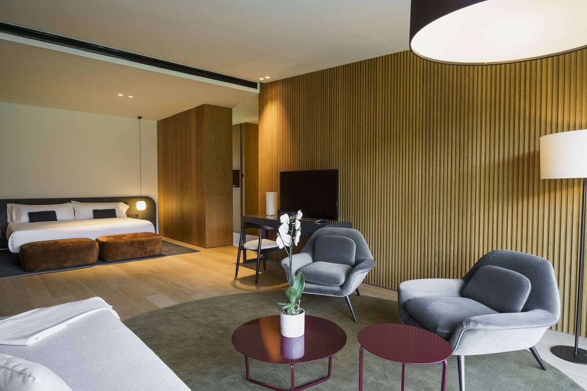 A modern hotel room with a bed, a desk, a chair, a sofa, and a lamp.