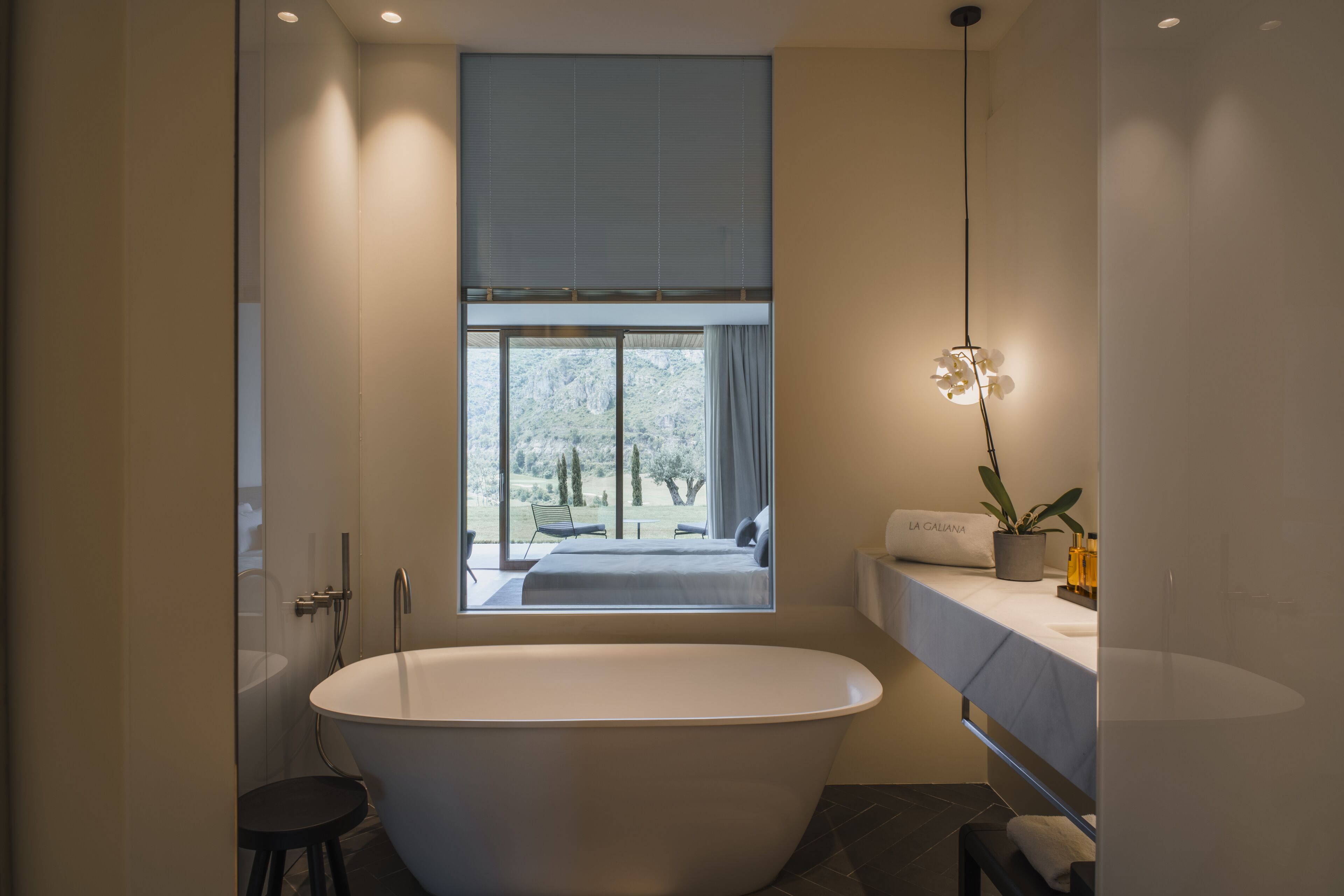 A modern bathroom with a freestanding bathtub, a window with a view of a garden, and a small stool.